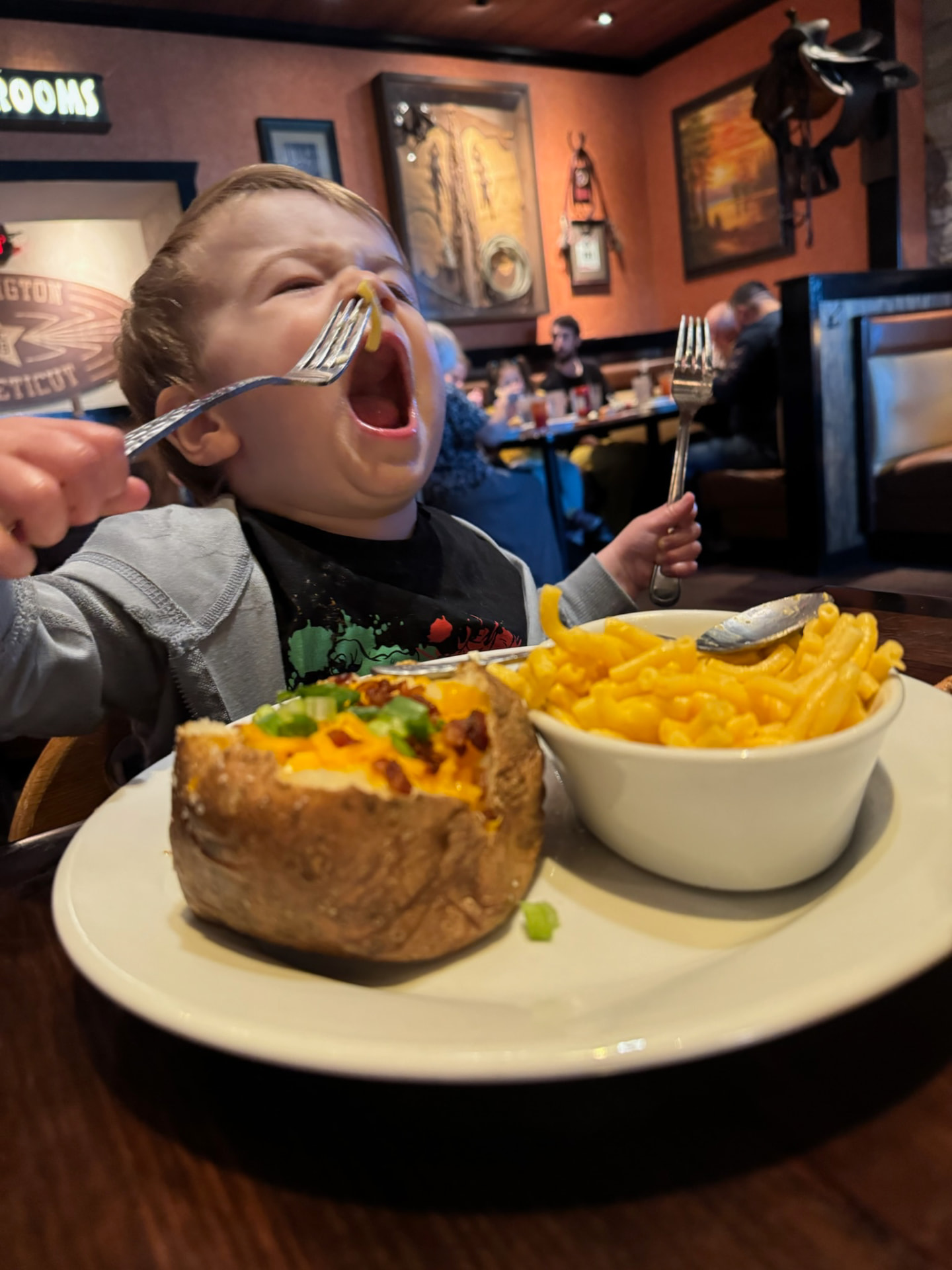 Brayden mid-giggle at a restaurant table with a forkful of mac and cheese
